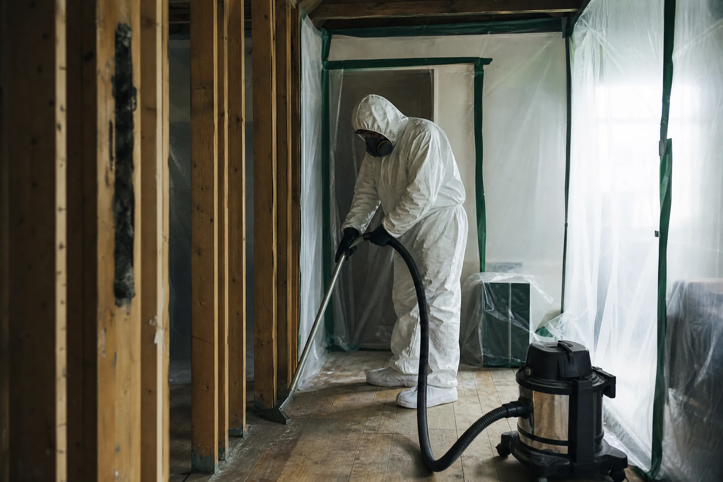 Technician HEPA-vacuuming cleaned wood framing inside containment