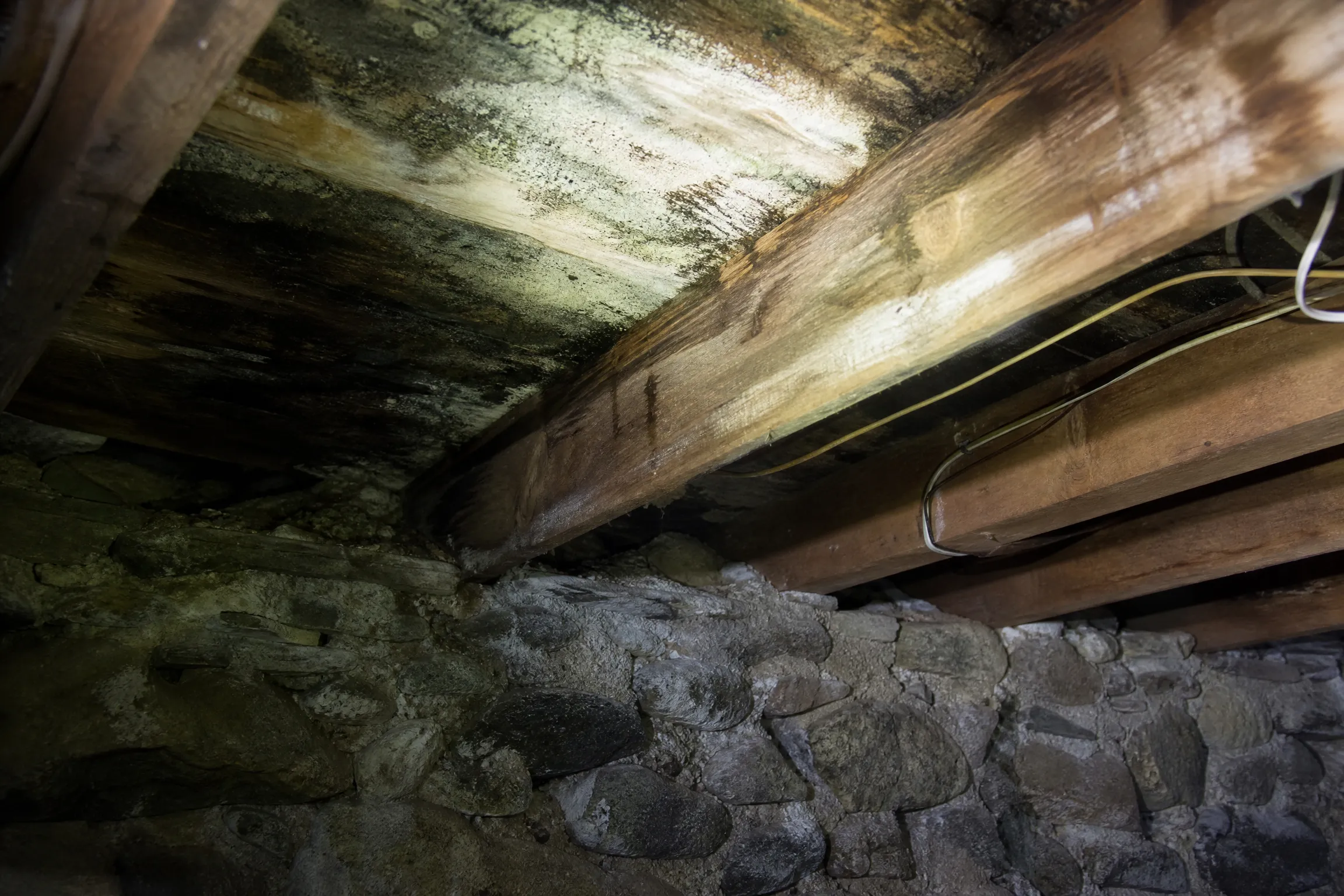 Mold growth on basement floor joists above a stone foundation